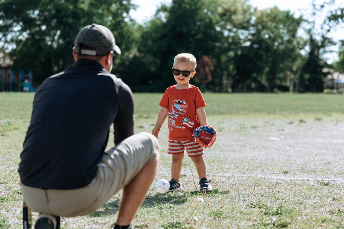 A father and young son playing baseball together in a park